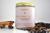 Cinnamon chai latte candle in a jar surrounded by cinnamon sticks and chai tea mix. 